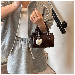 Dettaglio di una borsa Boston in pelle verniciata marrone con ciondolo a cuore di perla