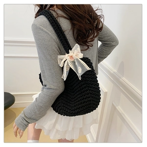 Detail of black knit tote bag featuring white lace bow and a delicate pink flower accent