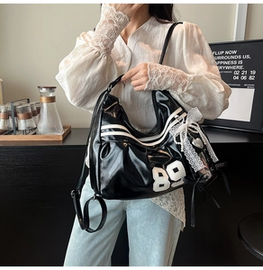 Détail du sac noir brillant avec écusson 89 blanc, dentelle et détails de chaîne en perles