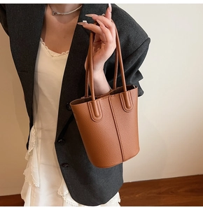 Brown bucket bag with lychee grain texture shown on a model wearing a grey blazer