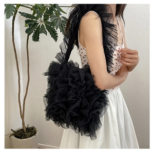 Detailed side view of black pleated lace shoulder tote bag on a model in minimalist room
