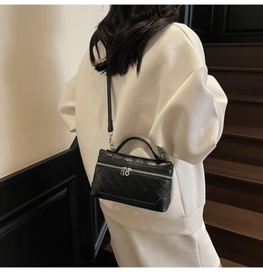 Detail of black quilted crossbody bag with silver zippers and elegant hand-carry handle