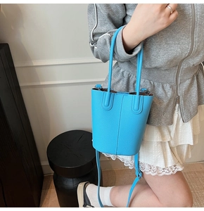 Detail of sky blue litchi grain leather bucket bag with top handles and adjustable strap