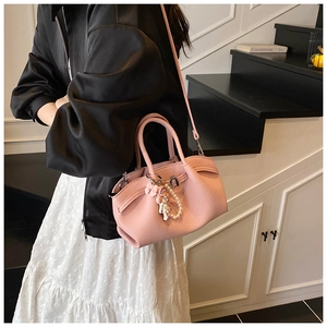 Detail view of pink lychee grain leather handbag with pearl charm and cute doll pendant