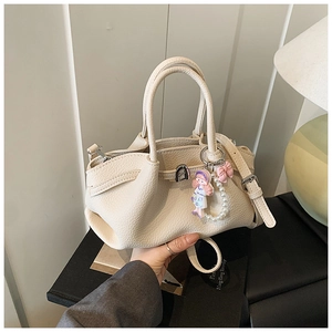 Close-up of beige lychee textured leather bag with bow and cartoon girl charm