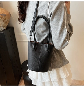 Detail of black lychee grain leather bucket bag showing dual handles and shoulder strap