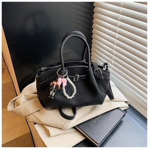Detail of black lychee grain leather handbag with cute doll pendant and silver buckle