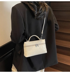 Detail of a quilted white leather crossbody bag worn over a formal black blazer
