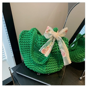 Close-up of a green woven tote bag with a white floral lace bow and embroidery