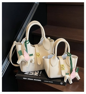 Détail du sac seau en cuir litchi crème avec fermoir doré et breloque pégase