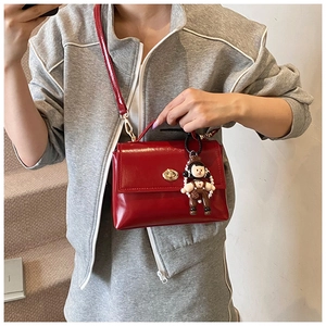 Dettaglio borsa in pelle cerata rossa con chiusura a scatto dorata e ciondolo a pupazzo
