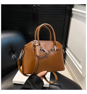Detail of a brown leather handbag featuring a metallic buckle and chain on a white display box
