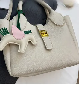 Détail du sac seau en cuir grainé crème avec fermoir rotatif en métal et pendentif pégase