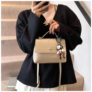 Dettaglio borsa beige in pelle cerata con chiusura dorata e ciondolo a forma di scimmia