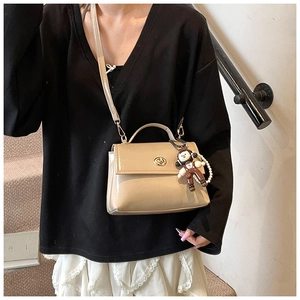 Dettaglio borsa beige in pelle cerata con chiusura dorata e ciondolo a forma di scimmia