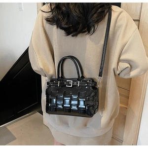 Dettaglio della trama in pelle nera intrecciata di una borsa a secchiello portata a spalla