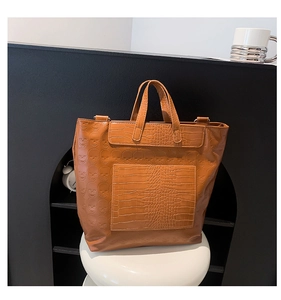 Close-up of brown crocodile texture tote bag with skull pattern on a white stool