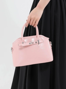 Pink polished leather handbag with top handles and silver buckle details on black background