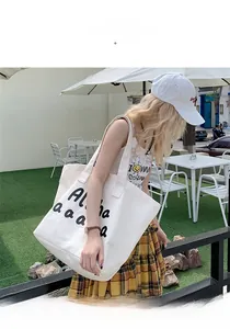 Detail of a large white canvas tote bag with black Aloha lettering in an outdoor setting