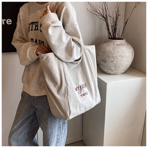 Close-up of canvas tote bag with you merci lettering showing texture and size on model