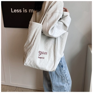 Minimalist canvas tote bag with red eyou merci text shown in a casual lifestyle setting