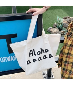 Detail of white canvas tote bag with black Aloha print in an outdoor casual setting