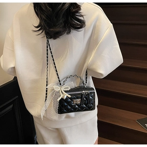 Detail of black quilted leather box bag with pearl lace bow and metal chain strap
