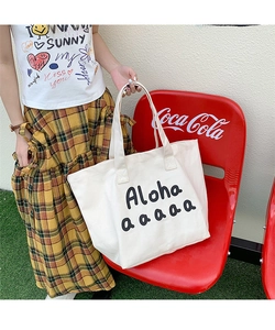 Close-up of white canvas tote bag featuring Aloha text print in a casual outdoor setting