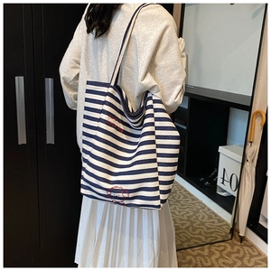 Detail view of blue and white striped canvas tote bag with cute dog embroidery on a shoulder
