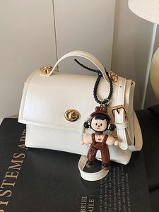 Borsa a mano bianca minimalista in pelle cerata con chiusura dorata e ciondolo a bambola