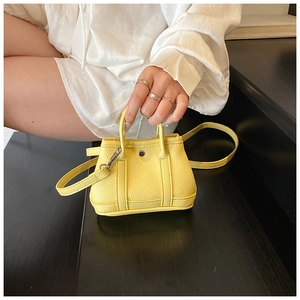Close-up of bright yellow mini crossbody bag with litchi texture held by a model