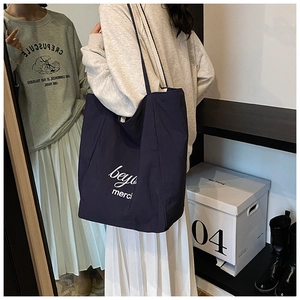 Detail view of large navy blue embroidered canvas tote bag with white merci lettering print