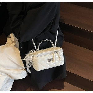 Detail of white quilted crossbody bag with pearl charms and lace detail on wooden steps