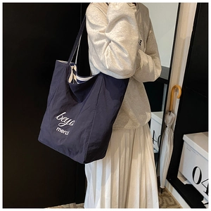 Detail of navy blue canvas tote bag featuring white merci embroidery and striped lining