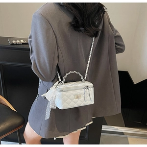 Detail of quilted white vanity bag with silver handle, lace bow, and pearl charm