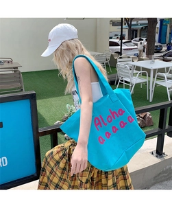 Outdoor lifestyle shot of sky blue canvas tote bag with pink Aloha printed design