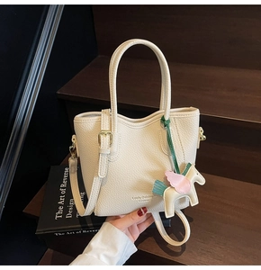 Detail of off-white lychee leather bucket bag with horse charm on wooden background