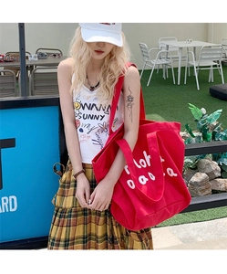 Detail of a large red canvas tote bag with white aloha text shown in a casual outdoor setting