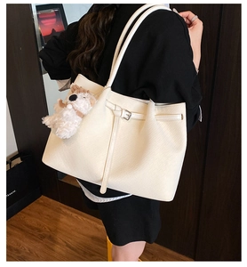 Detail view of woven leather tote bag with plush puppy pendant on a model's shoulder