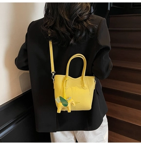 Detail of yellow litchi leather handbag featuring a cute horse charm and brand embossing