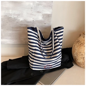 Detail view of a striped canvas tote bag featuring a red puppy embroidery in a cozy setting