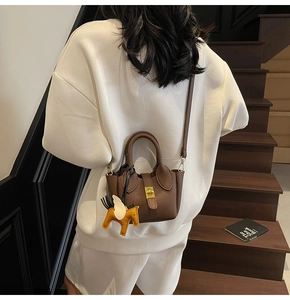 Détail d'un sac seau marron à motif litchi avec breloque cheval porté par un mannequin