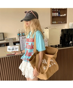 Close-up of a large khaki canvas tote bag with white lettering in a cafe setting