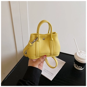 Detail of a bright yellow mini handbag in lychee leather with metal buckles and strap