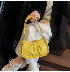 Detail of a bright yellow pleated hobo bag with a woven handle worn by a model in a black blazer