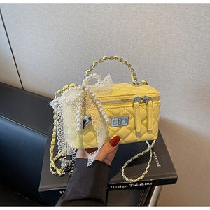 Close-up of yellow quilted bag featuring pearls, lace bow, and silver heart charm details