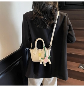 Détail du sac seau en cuir crème avec texture grainée et charm en forme de cheval
