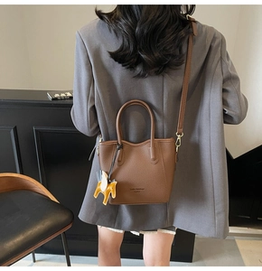 Deep brown lychee pattern leather bucket bag with horse charm on a modern background