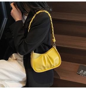 Detail of yellow pleated crescent bag with braided strap and lychee grain leather