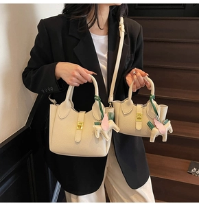 Détail de sacs seaux en cuir grainé blanc cassé avec fermoirs dorés et breloques cheval